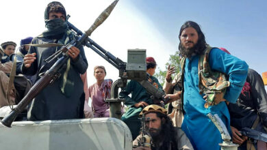 Taliban fighters sit over a vehicle on a street in Laghman province
