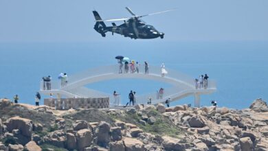 Tourists look on as a Chinese military helicopter flies past Pingtan island, one of mainland China's closest points to Taiwan, in Fujian province on Thursday, ahead of massive military drills off Taiwan