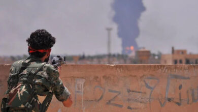 A Kurdish fighter with the People's Protection Units (YPG) looks on at an air strike in the distance