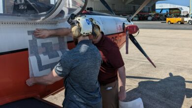 Engineers from the Naval Air Warfare Center Aircraft Division apply a fiducial tag aboard a T-6 Texan to autonomously capture arrival and departure data during ground operations in an experiment at Naval Air Station Patuxent River, Maryland in 2022. (U.S. Navy photo)