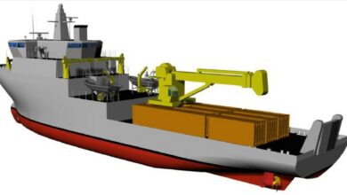 A 3D rendering of the Coastal Motor Transport and Lighthouse Servicing (MTC/MTF) ship. The image shows some of the major components of the vessel: the hull painted mostly in gray except for the bottom part which is red, the heavy machinery cranes colored in yellow, and the shipping containers on the dock colored orange.