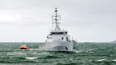 Cayor, a 58 S-class offshore patrol vehicle, is seen sailing in green-blue waters. The gray seacraft is accompanied by a much smaller red boat, which is sailing on its right side.
