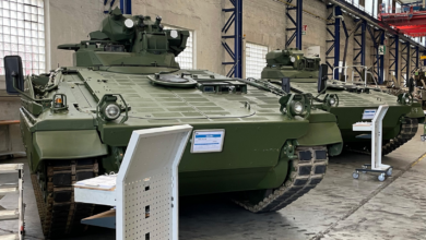 Two Marder 1A3 Infantry Fighting Vehicles are seen displayed inside a warehouse-like building. The vehicles are painted dark green.