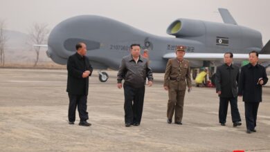 North Korean leader Kim Jong Un walking with cohorts with a suicide drone in the background