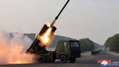 An M1991 Multiple Launch Rocket System (MLRS) is seen launching a rocket from one of its barrels. The launcher is on the back of the unit's truck component.