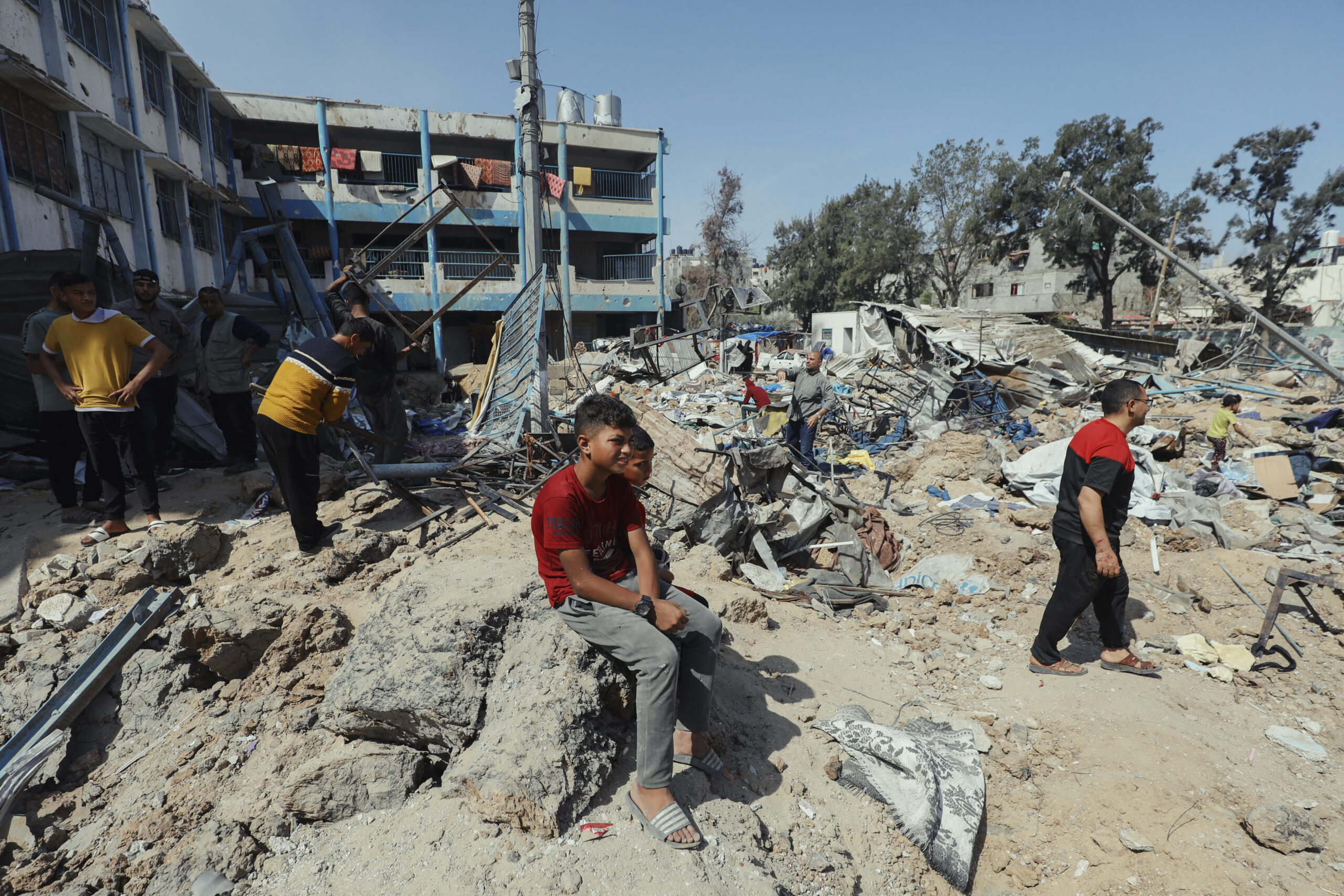 People walk through rubble and debris outside Abu Hamisa School in Al-Bureij camp, Gaza, on May 10, 2025. The school, used as a shelter for displaced families, was bombed twice on the same day several days ago. (Photo by Moiz Salhi / Middle East Images / Middle East Images via AFP)
