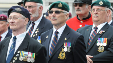 A group of British Armed Forces veterans are seen grouped together on a parade. They are all wearing suits and medals, as well as berets.