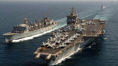 The warship USS Enterprise is seen sailing across deep blue waters. The aircraft carrier has dozens of fighter planes and a helicopter taxied on it.