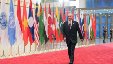 Vladimir Putin walking over a red carpet with country flags in the background
