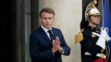 French President Emmanuel Macron rubbing his hands with a royal guard in the backgorund