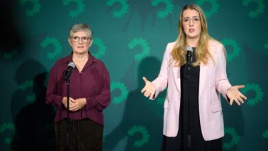 Britta Haßelmann wearing a maroon blouse, and Katharina Dröge wearing a light pink blazer over a black dress while speaking at a press conference with a green background
