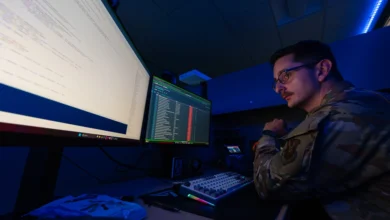 A soldier in a dark room looking at two monitors