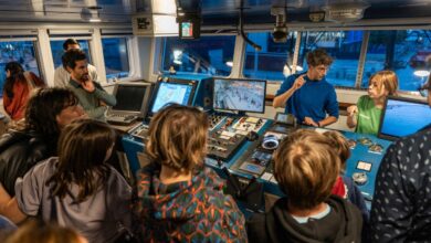 Greenpeace activists on a boat, gathered around a laptop, engaged in a discussion about environmental initiatives