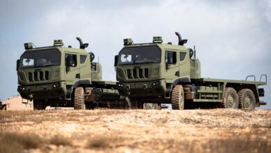 A brightly lit photo of two green trucks with the Naviground system with a light brown soil surface