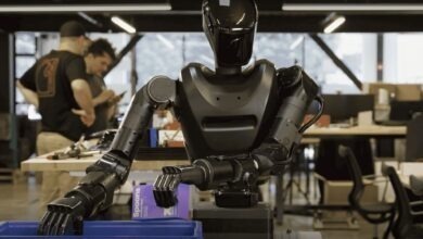 Humanoid robot operating in a robotics lab, using articulated arms to handle objects while engineers work in the background
