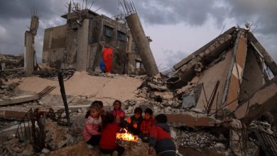 Displaced Palestinians warm up by the fire after their homes are destroyed following heavy rain in Gaza City, Palestine, on January 14, 2026.