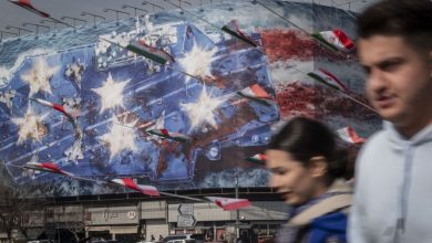 Iranian youths walk past a state building covered with a giant anti-US billboard depicting a symbolic image of the destroyed USS Abraham Lincoln (CVN-72) aircraft carrier in downtown Tehran, Iran, on January 28, 2026.