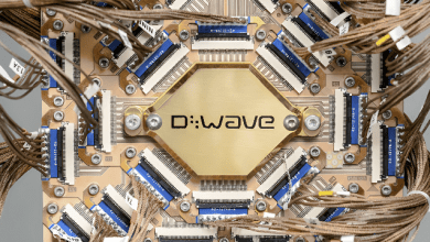 Close-up of a D-Wave quantum processor chip mounted on a copper-colored circuit assembly, with dense wiring and connectors surrounding the central quantum module.