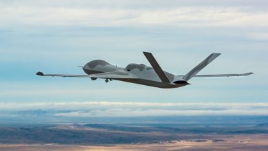 MQ-20 Avenger drone flying at altitude over a desert landscape, showing its stealthy blended-wing design, rear-mounted engine, and long wingspan during an autonomous flight demonstration.