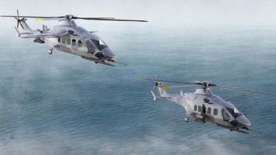 Two gray camouflage Airbus military helicopters fly in formation over a calm ocean beneath an overcast sky.