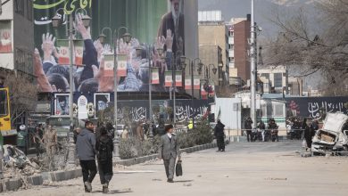 Iranian people walk through the area under a portrait of Iran's Late Leader, Ayatollah Ali Khamenei, outside a police facility that is completely destroyed during a US-Israeli military campaign in Tehran, Iran, on March 4, 2026.