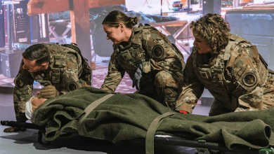 U.S. military personnel in OCP camouflage uniforms practicing trauma simulation casualty care on a litter during an indoor training exercise