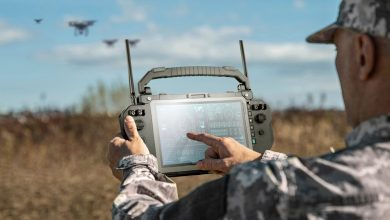 Soldier operating a Getac UX10 rugged ground control station touchscreen in an open field with multiple military drones visible in the background, illustrating a modular unmanned systems command center