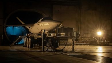Kratos XQ-58 Valkyrie stealth drone displayed on a wheeled trailer inside a military hangar during low-light pre-flight or testing operations, co-branded with Airbus