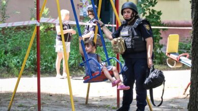 A psychologist with the State Emergency Service of Ukraine stands beside a girl on a swing near a five-storey residential building damaged by a missile strike in Kharkiv, Ukraine