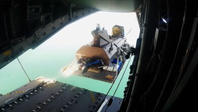 A Kraken K3 Scout uncrewed surface vessel (USV) attached to a Capewell UMCADS delivery platform being jettisoned from the open rear cargo ramp of an Airbus A400M military transport aircraft over the ocean.